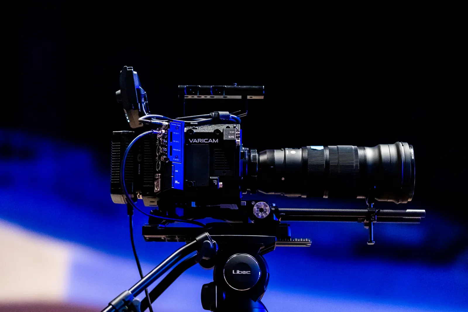 Side view of a professional video camera with lens on a tripod, ready for filming.