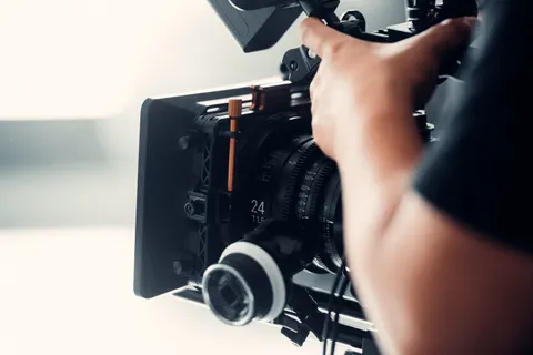 Eine Person bedient bei einem Dreh in Innenr&auml;umen eine professionelle Videokamera.