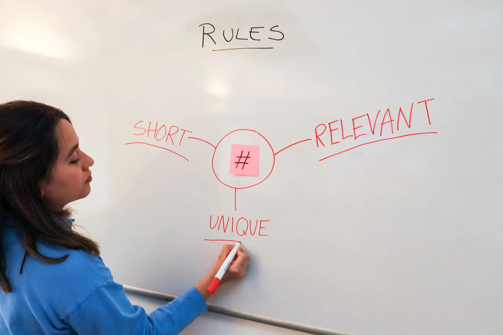 Woman illustrating marketing rules with hashtags on a whiteboard for effective branding strategies.