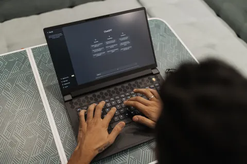 Nahaufnahme von H&auml;nden, die in einem Innenraum auf einem Laptop mit der ChatGPT-Oberfl&auml;che tippen.