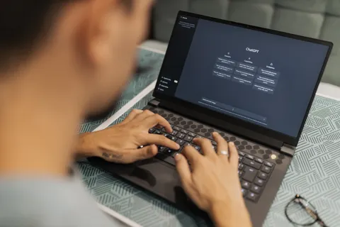 Eine konzentrierte Person tippt in einem Innenraum auf einem Laptop, auf dem KI-Software l&auml;uft.