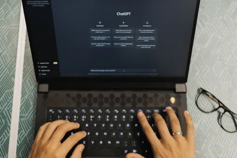 H&auml;nde tippen auf einem Laptop mit ge&ouml;ffnetem ChatGPT, Thema kabellose Technologie.