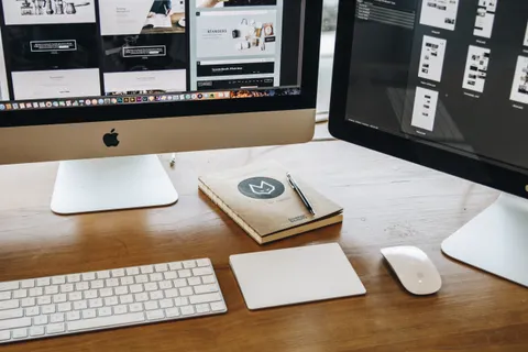 Ein minimalistischer Schreibtisch mit zwei Monitoren, Tastatur, Maus und Notizbuch f&uuml;r produktives Arbeiten.