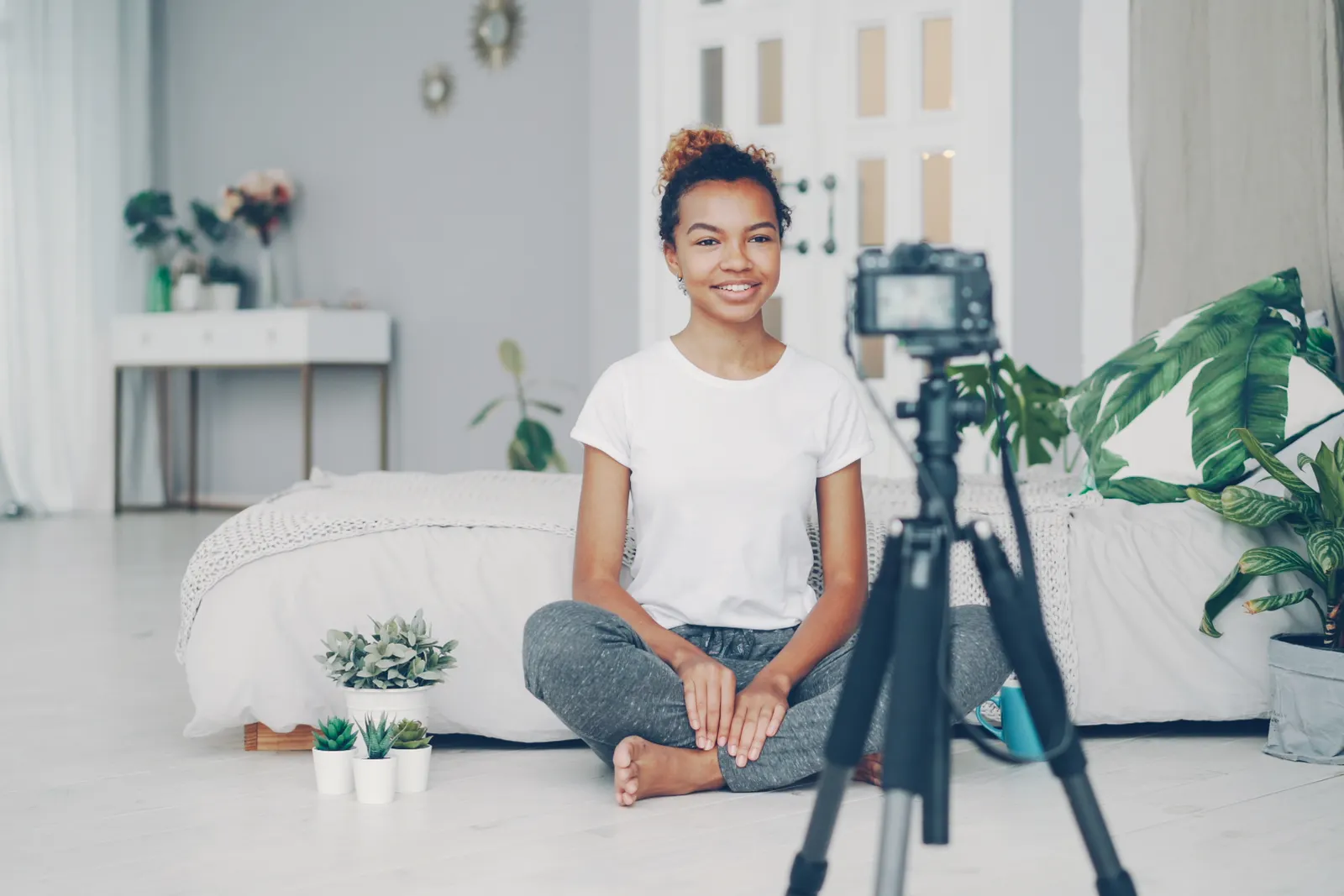 Smiling woman filming a vlog in cozy indoor setting with plants and soft lighting.