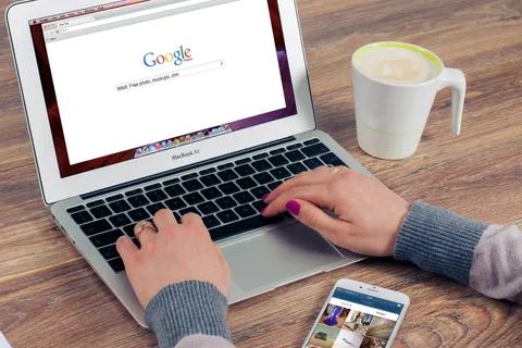 H&auml;nde tippen auf einem MacBook Air mit ge&ouml;ffneter Google-Suche, daneben ein Kaffee.