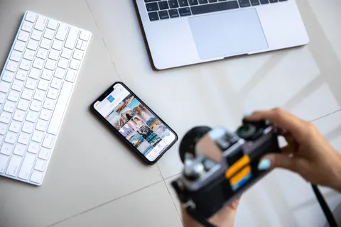 Person nutzt eine Vintage-Kamera zusammen mit Smartphone und Laptop in einem kreativen Setup.