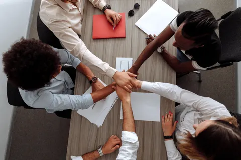 Draufsicht auf ein vielf&auml;ltiges Team, das in einem Meeting als Zeichen der Einigkeit die H&auml;nde zusammenlegt.