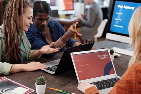 Ein vielf&auml;ltiges Team arbeitet in einem modernen B&uuml;ro mit Laptops zusammen und spricht &uuml;ber den digitalen Wandel.