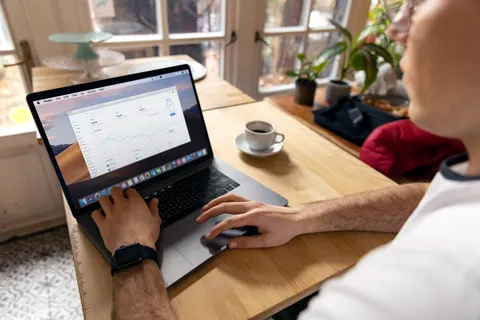 Eine Person arbeitet in gem&uuml;tlicher Umgebung an einem Laptop mit Gesch&auml;ftsanalysen, ein typischer Remote-Arbeitsplatz.