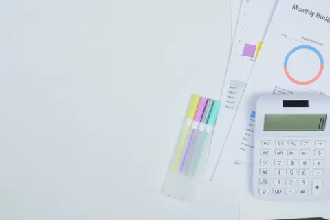 Minimalistischer Schreibtisch mit Taschenrechner, Unterlagen zur Budgetplanung und bunten Stiften.