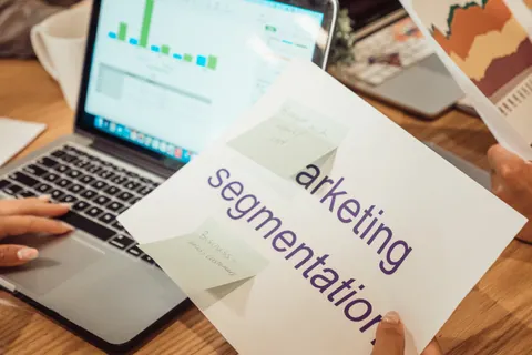 Ein moderner Arbeitsplatz: H&auml;nde analysieren Marketingdaten auf einem Laptop und in Papierunterlagen.