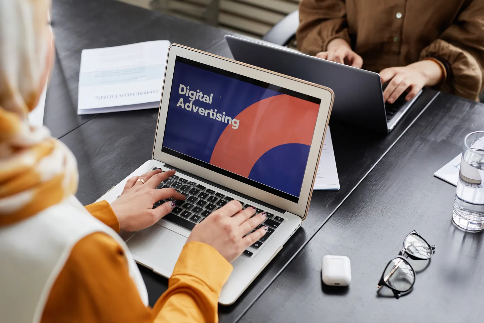 Two professionals work on laptops focusing on digital advertising in an office setting.